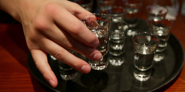 Eine Hand greift in einer Gaststätte nach einem gefüllten Schnapsglas.