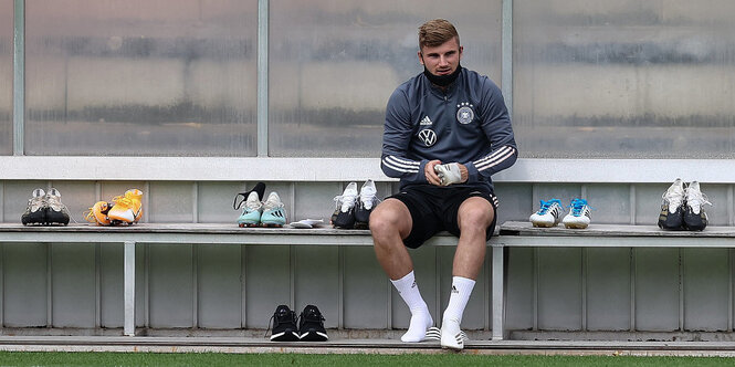 Timo Werner beim Training. Er sitzt mt Mund-Nasen-Schutz auf der Bank und hat ein paar Schuhe in der Hand. Außer ihm sitzt niemand auf der Bank. Nur einige Schuhpaare stehen darauf.