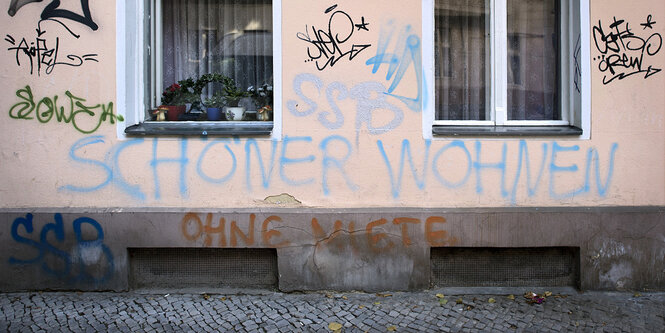 Die Wand von einem Haus. Unter zwei Fenster wurde mit Graffiti geschrieben: Schöner Wohnen ohne Miete.