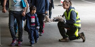 Eine Frau, die eine gelbe Warnweste trägt, reicht einem Kind ein Stofftier