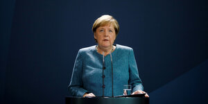 Angela Merkel steht an einem Rednerpult und spricht vor einem blauen Hintergrund