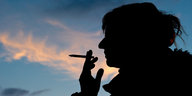 Silhouette einer rauchenden Frau vor Abendhimmel