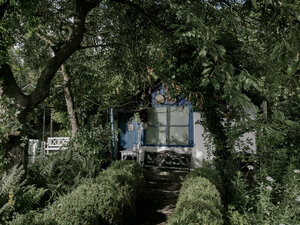 Eine Gartenlaube mit blauer Tür versteckt hinter Bäumen