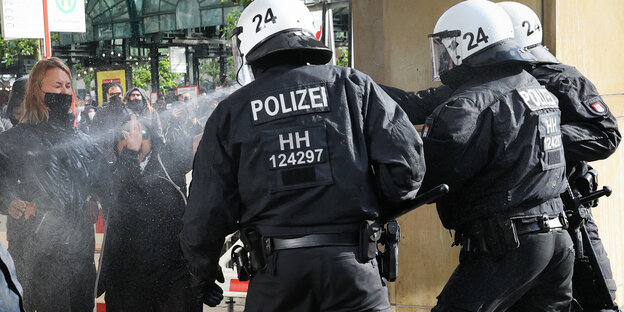Behelmte Polizisten sprühen Flüssigkeit auf Demonstranten
