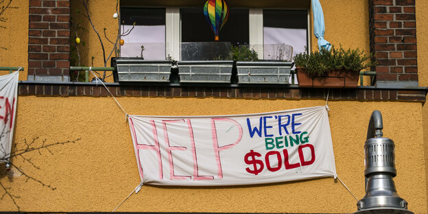 Ein Banner an dem Balkon eines Mietshauses. Drauf steht: "Help! We're being sold"