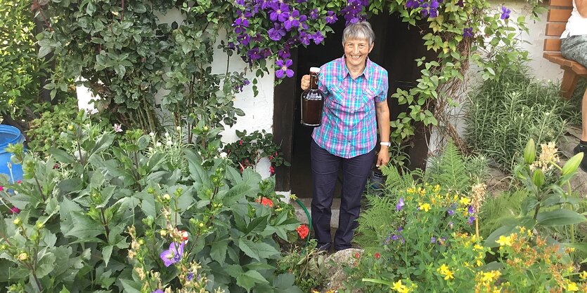 Eine Frau kommt mit einer Flasche aus einem von Blumen umrankten Kellereingang