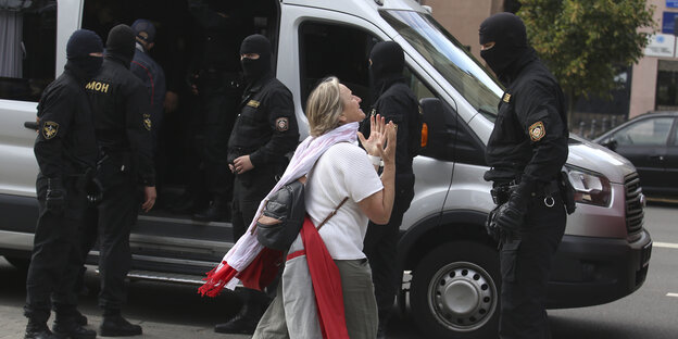 Eine Frau mit Belarus-Fahne und ein maskierter Polizist vor einem Streifenwagen