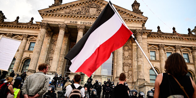 Teilnehmer einer Kundgebung gegen die Corona-Maßnahmen stehen vor dem Reichstag, ein Teilnehmer hält eine Reichsflagge.