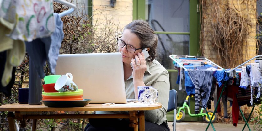 Eine Frau sitzt im Garten am Computer, nebendran hängt Wäsche