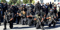 Vermummte, bewaffnete, schwarz gekleidete Menschen posieren für ein Foto.