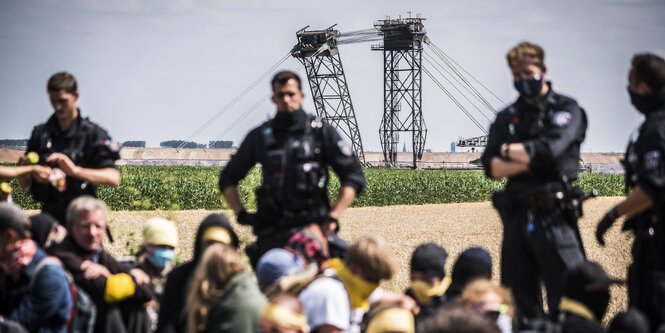Polizisten halten eine Gruppe am Boden sitzende Demonstranten in Schach