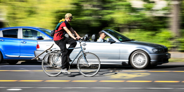 Ein Mann radelt auf einem Pop-Up Fahrradweg auf der Straße, auf der Autospur fährt ein Cabriolet