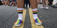 Ein Menschmit Schuhen in Regenbogenfarben und bunten Socken stehet auf der Strasse