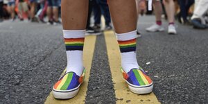 Ein Menschmit Schuhen in Regenbogenfarben und bunten Socken stehet auf der Strasse