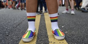 Ein Menschmit Schuhen in Regenbogenfarben und bunten Socken stehet auf der Strasse