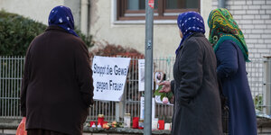 Drei Frauen stehen vor Kerzen und einem Schild, auf dem "Stoppt die Gewalt gegen Frauen" steht