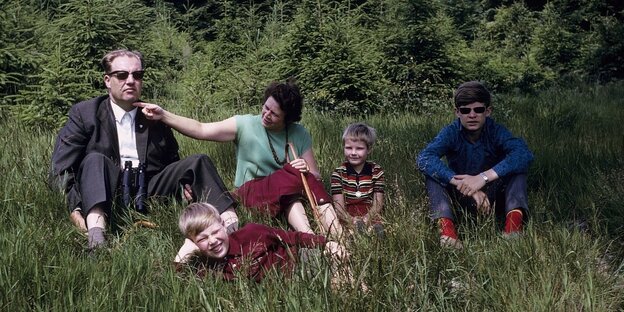Eine Familie sitz im Gras, der Vater schaut missmutig, die Mutter streicht ihm über das Kinn