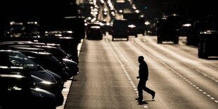 ein Mann läuft über die Strasse. Am Strassenrand und im Hintergrund sind Autos.