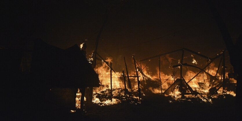 Vor dem dunklen Nachthimmel schlagen Flammen aus Gebäuden.