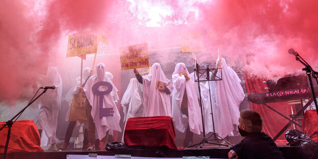Als Gespenster verkleidete Menschen stehen auf einer Bühne in rotem Rauch