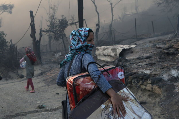 Eine Frau trägt schwere Taschen, blickt ängstlich über die Schulter und läuft durch eine ausgebrannte Landschaft