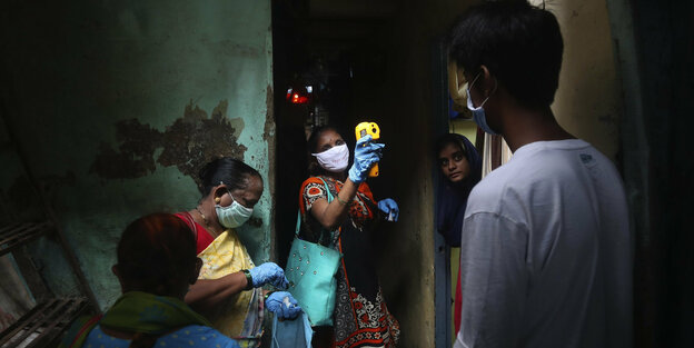 Gesundheitsarbeiterin in einem Slum misst an der Haustür Fieber mit einer Art Pistole.