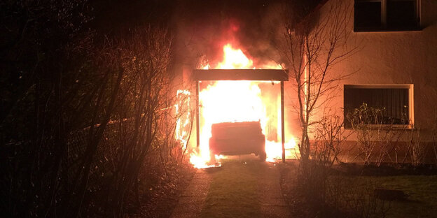 Ein brennendes Auto steht dicht neben einem Wohnhaus. Die Flammen drohen aufs Haus überzugreifen.