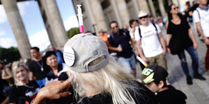 Ein Teilnehmer trägt eine Kappe mit einer Spritze und einem Button "Querdenken 711 Stuttgart" am Brandenburger Tor bei einer Demonstration gegen die Corona-Maßnahmen.