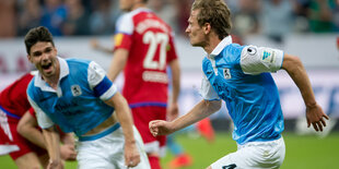 zwei Fußballspieler in weiß-blau jubeln, dahinter trotten zwei in rot davon.