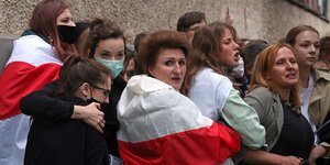 Frauen stehen nebeneinander, eine hat die Fahen der belarussischen Opposition um die SChulter gelegt