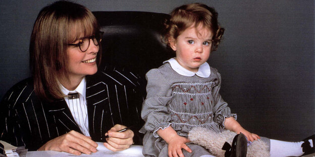 Diane Keaton sitzt lächelnd neben ihrem Baby im Film Baby Boom