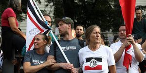 Menschen stehen in einer Gruppe beieinader, eine Frau trägt ein T-shirt, auf dem eine Reichsfahne gedruckt ist