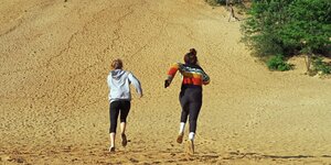 Zwei Frauen in Sportbekleidung laufen eineaufsteigende Sandfläche im Grunewald empor.