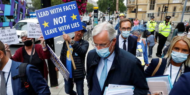 Mann mit Mundschutz inmitten von Protestlern mit Plakaten in EU-Blau.