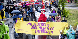 Menschen laufen in regenkleidung auf einer Demo durch die Straße