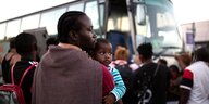 Ein Mann hält ein Kind auf dem Arm und wartet daruf, in einen Bus einsteigen zu können