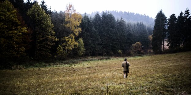 Ein Jäger mit Gewehr an der Schulter steht allein am Waldrand auf einem Stoppelfeld
