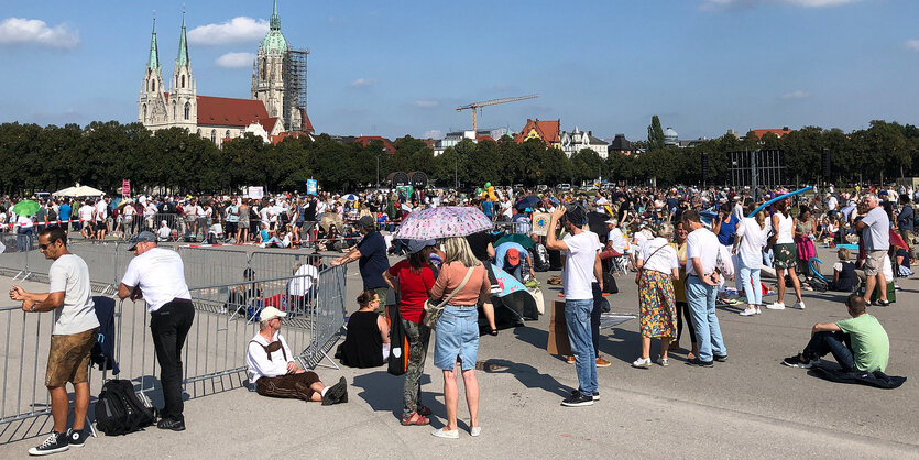 Viele Menschen auf der Theresienwiese bei weiß-blauem Himmel, im Hintergrund eine eingerüstete Kirche