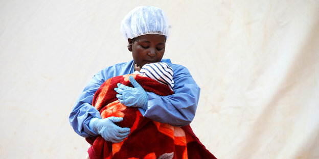 Eine Frau in Schutzkleidung im Kongo hält ihr Baby im Arm.