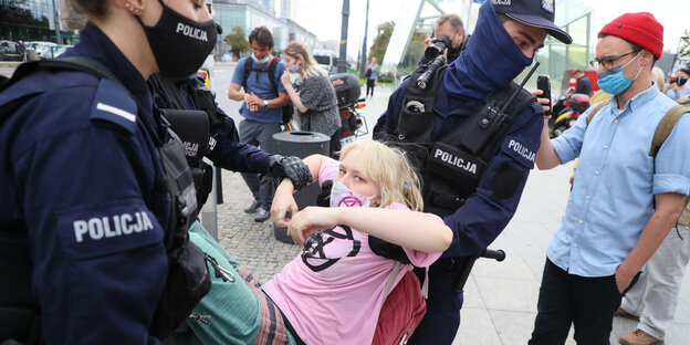 Frau mit Extinction-Rebellion-Shirt wird von Polizist:innen weggetragen