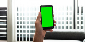 Ein Mann liegt auf dem Sofa und schaut in ein Smartphone mit grünem Bildschirm