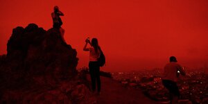 Leute blicken auf eine in rotes Zwielicht gehüllte Stadt und machen Fotos