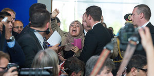 Eine Frau hebt den Arm und schreit umgeben von Journalisten und Sicherheitsleuten