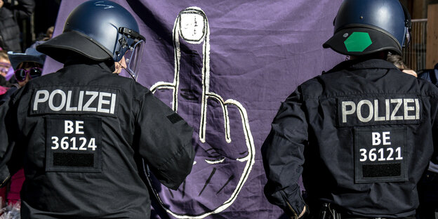 Ein Transparent mit einem Mittelfinger bei einer Demonstration vor Polizisten.