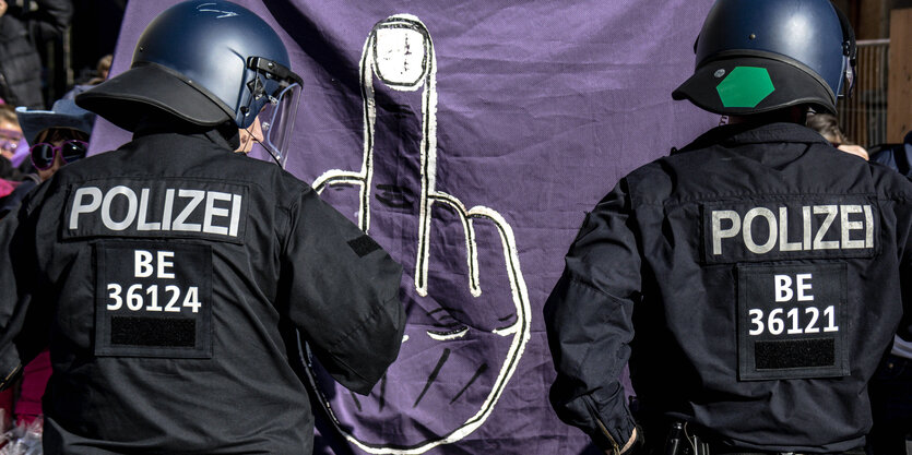 Ein Transparent mit einem Mittelfinger bei einer Demonstration vor Polizisten.