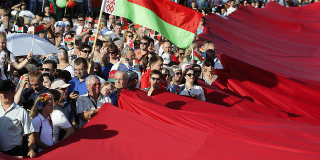 Unterstützer von Lukashenko halten gemeinsam eine riessige belarusische Flagge