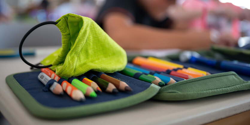 Ein Mund- und Nasenschutz liegt am ersten Schultag des neuen Schuljahres in einer Grundschule auf einem Mäppchen. Unter Ausnahmebedingungen und ungewissen Vorzeichen starten 1,5 Millionen Schüler und mehr als 135 000 Lehrer in ein neues Schuljahr.