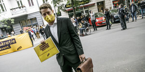 Ein Mann mit Anzug und Lederaktentasche geht über eine Straße: Er trägt Mundschutz und reicht Klage beim Berliner Verwaltungsgericht ein