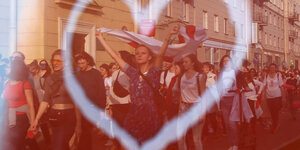 Demonstrantinnen mit rot-weißen Flaggen in Minsk werden in einem Fenster mit Herz-Symbol reflektiert