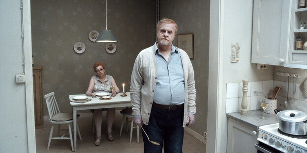 Eine Frau und ein Mann in eienr Küche blicken in Roy Anderssons Film "Über die Unendlichkeit" in die Kamera.
